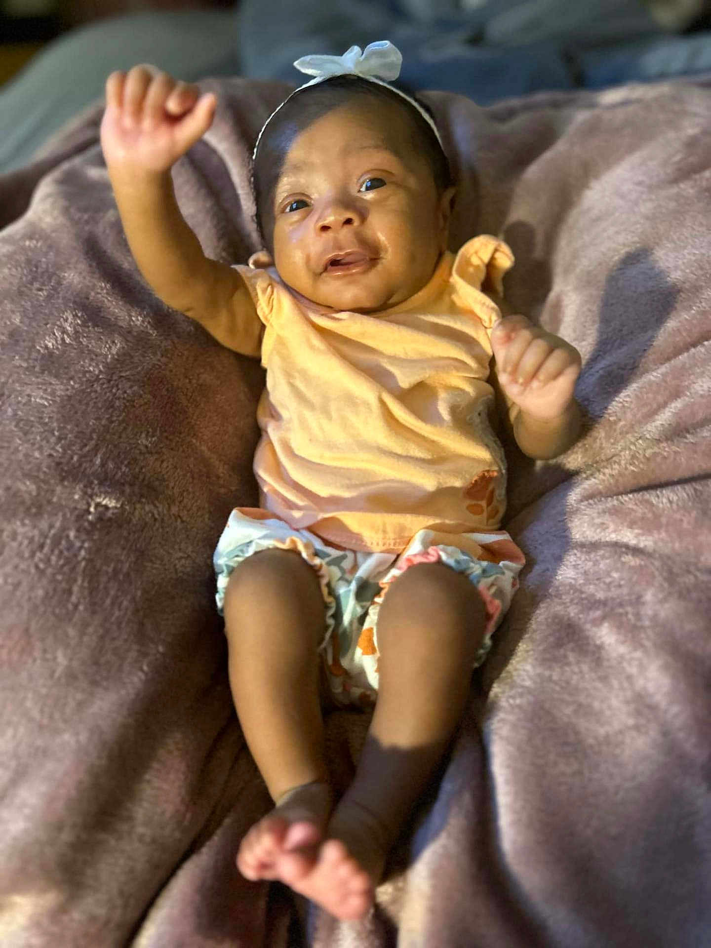 Yahari is registered to the contest to win money with this photo: baby, infant, child, smiling, headband, orange_clothing, blanket, soft_texture, happy, raised_arm, bare_feet, cute, lying_down, indoors, portrait, person, skin, toddler, small_person, cozy