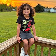 Paris joined the competition — help win amazing prizes! child, smiling, curly_hair, sunset, outdoor, grass, wooden_railing, casual_clothing, black_tshirt, denim_skirt, white_sneakers, green_field, trees, sky, nature, happy, portrait, daylight, person, young