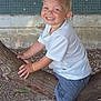 child, boy, smiling, blonde_hair, blue_eyes, tree_branch, outdoor, casual_clothing, white_tshirt, blue_shorts, white_sneakers, playful, nature, dirt_ground, wall, tiles, rustic, happy, person, daylight