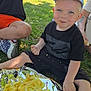 toddler, child, picnic, potato_chips, grass, foil, cap, blue_eyes, black_tshirt, orange_shorts, sippy_cup, outdoor, sunlight, happy, smiling, food, snack, person, nature, casual_clothing