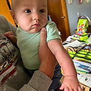 Lawrence joined the competition — help win amazing prizes! baby, infant, person, hand, clothing, indoor, adult_hand, face, expression, sleeve, door, furniture, room, paper, colorful, casual, holding, skin, curious, young_child