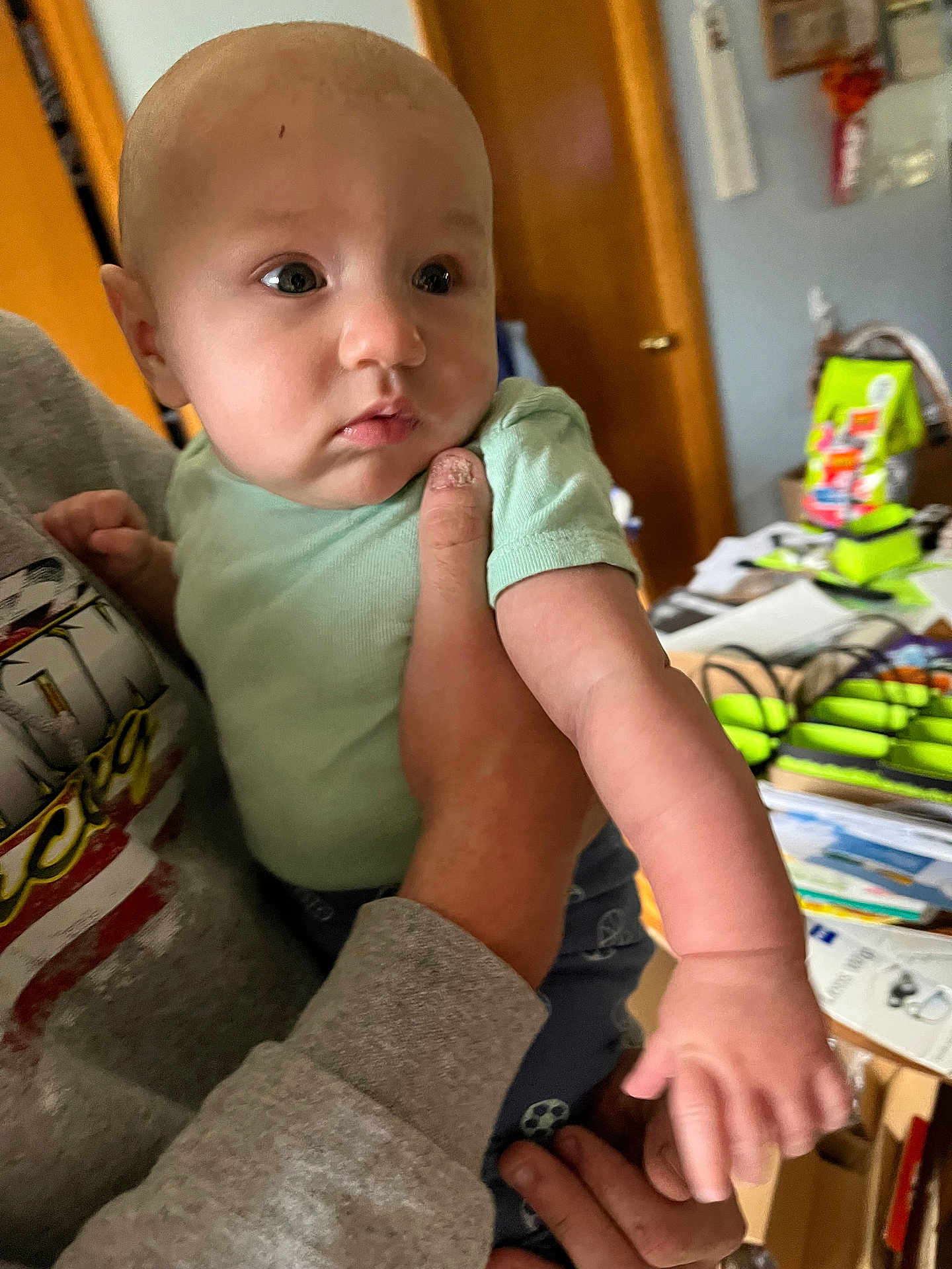 Lawrence joined the competition — help win amazing prizes! baby, infant, person, hand, clothing, indoor, adult_hand, face, expression, sleeve, door, furniture, room, paper, colorful, casual, holding, skin, curious, young_child