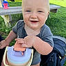 Benny is registered to the contest to win money with this photo: baby, child, smiling, happy, portrait, outdoor, grass, picnic, bench, sippy_cup, stroller, infant, blue_eyes, blond_hair, gray_shirt, sitting, close_up, daylight, park, family