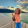 Giulia participe au concours pour gagner de l'argent avec cette photo : casual_clothing, child, clouds, cute, fashion, girl, handbag, happy, jeans, lake, mountains, nature, orange_top, outdoor, pier, portrait, smiling, sunset, water, wooden_boardwalk