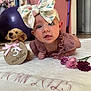 baby, bow, flower, plush_dog, blanket, clothing, infant, face, headwear, pink, purple, room, toy, soft_toy, tummy_time, cute, child, indoor, decor, portrait