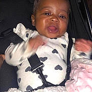 Jadiyah is registered to the contest to win money with this photo: baby, child, car_seat, seatbelt, clothing, white, black_hearts, blanket, pink_blanket, happy, smiling, face, infant, person, indoors, cute, young, portrait, hands, car_interior