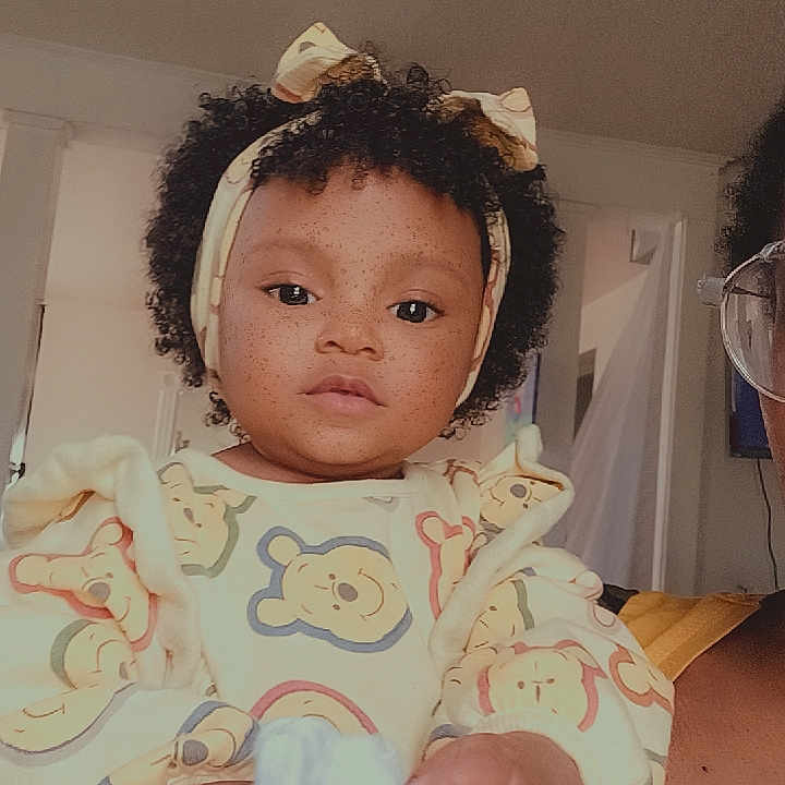 Sámone is registered to the contest to win money with this photo: bear, bow, child, clothing, curly_hair, cute, expression, fabric, face, furniture, hand, headband, holding, home, indoor, pattern, person, portrait, toddler, wall