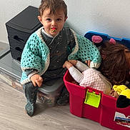 Logan Nonotte participe au concours pour gagner de l'argent avec cette photo : toddler, child, blanket, crochet, toy_box, doll, plush_toy, flooring, storage_box, snack, indoor, curly_hair, sitting, playtime, home, casual_clothing, curious, young_child, wood_floor, colorful