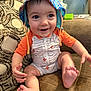 baby, child, smiling, hat, onesie, couch, indoor, happy, sitting, feet, hand, face, patterned_pillow, clothing, infant, cute, expression, living_room, furniture, colorful