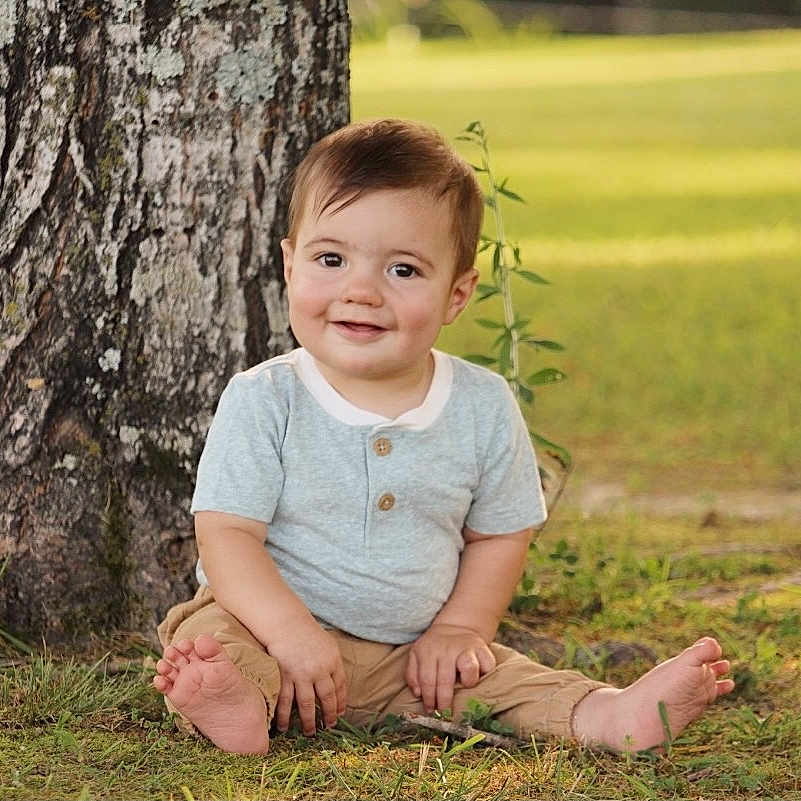 Carson joined the competition — help win amazing prizes! baby, barefoot, casual_clothing, child, cute, daylight, grass, greenery, happy, nature, one_person, outdoor, pants, portrait, short_sleeve, sitting, smiling, toddler, tree, young
