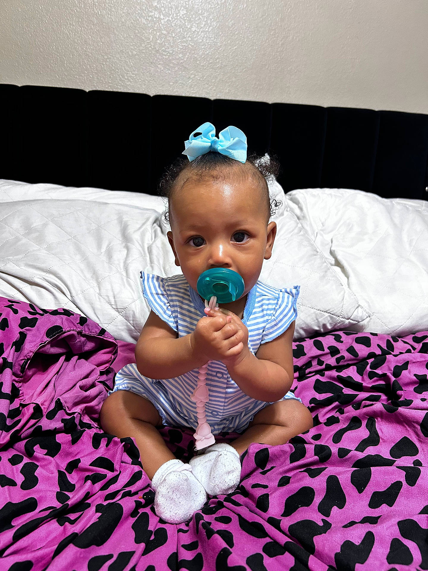 baby, bed, blanket, blue_bow, child, curious, cute, footwear, headwear, indoor, infant, pacifier, people, portrait, purple_blanket, sitting, socks, striped_outfit, white_pillow, young_child