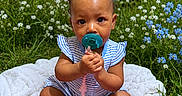 Keauni is registered to the contest to win money with this photo: baby, child, pacifier, blue_bow, striped_clothing, white_blanket, wildflowers, grass, outdoor, cute, sitting, infant, nature, greenery, blue_flowers, white_flowers, curly_hair, sock, summer, portrait