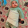 baby, child, infant, knitted_clothing, green_outfit, hat, blanket, lying_down, carpet, floral_pattern, indoors, cute, face, wide_eyes, rosy_cheeks, warm_clothing, patterned_rug, soft_lighting, portrait, cozy