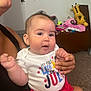 4th_of_july, adult, baby, carpet, celebration, child, clothing, cute, eyes, face, giraffe_plush, hand, indoor, infant, mouth, onesie, person, polka_dots, red_shorts, toys