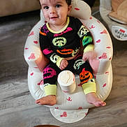 Ryland is registered to the contest to win money with this photo: baby, child, cute, face, flooring, foot, halloween, hand, happy, indoors, infant, inflatable_chair, pajamas, person, pink_candy_pattern, pumpkin, sitting, smiling, white_chair, wood_floor