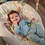 baby, infant, baby_seat, smiling, blue_onesie, toy, fingers_in_mouth, happy, indoor, flooring, wood_floor, cushion, child, person, face, head, home, foot, soft_toy, comfort