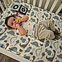 baby, crib, dinosaur_bedding, toy, socks, infant, child, floor, wood_floor, hand, clothing, sleepwear, cute, indoors, person, face, lying_down, playful, room, footwear