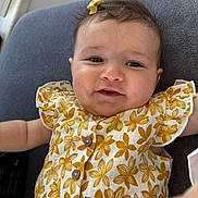 Jennah a rejoint le concours — aidez-le/la à gagner de superbes lots ! baby, child, smiling, face, hair_bow, dress, floral_pattern, cushion, button, indoor, closeup, cute, infant, person, skin, head, cheeks, eyes, arm, fabric