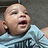 Princeston is registered to the contest to win money with this photo: baby, infant, child, portrait, close_up, face, wide_eyed, open_mouth, surprised, smiling, gray_shirt, nike, clothing, being_held, indoor, home, carpet, furniture, adorable, photography