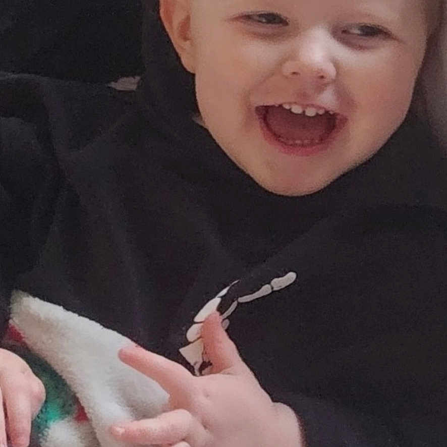 Allie Jo joined the competition — help win amazing prizes! bed, black_clothing, blanket, blonde_hair, casual, child, close_up, eyes, face, happy, indoor, laughing, phone_screenshot, pigtails, portrait, sitting, smiling, sweatshirt, teeth, toddler