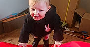 Allie Jo is registered to the contest to win money with this photo: black_clothing, blonde_hair, boots, cardboard, child, face, happy, household, indoor, moving_boxes, photography, pigtails, playful, portrait, red_play_surface, smiling, standing, toddler, toy, wooden_floor