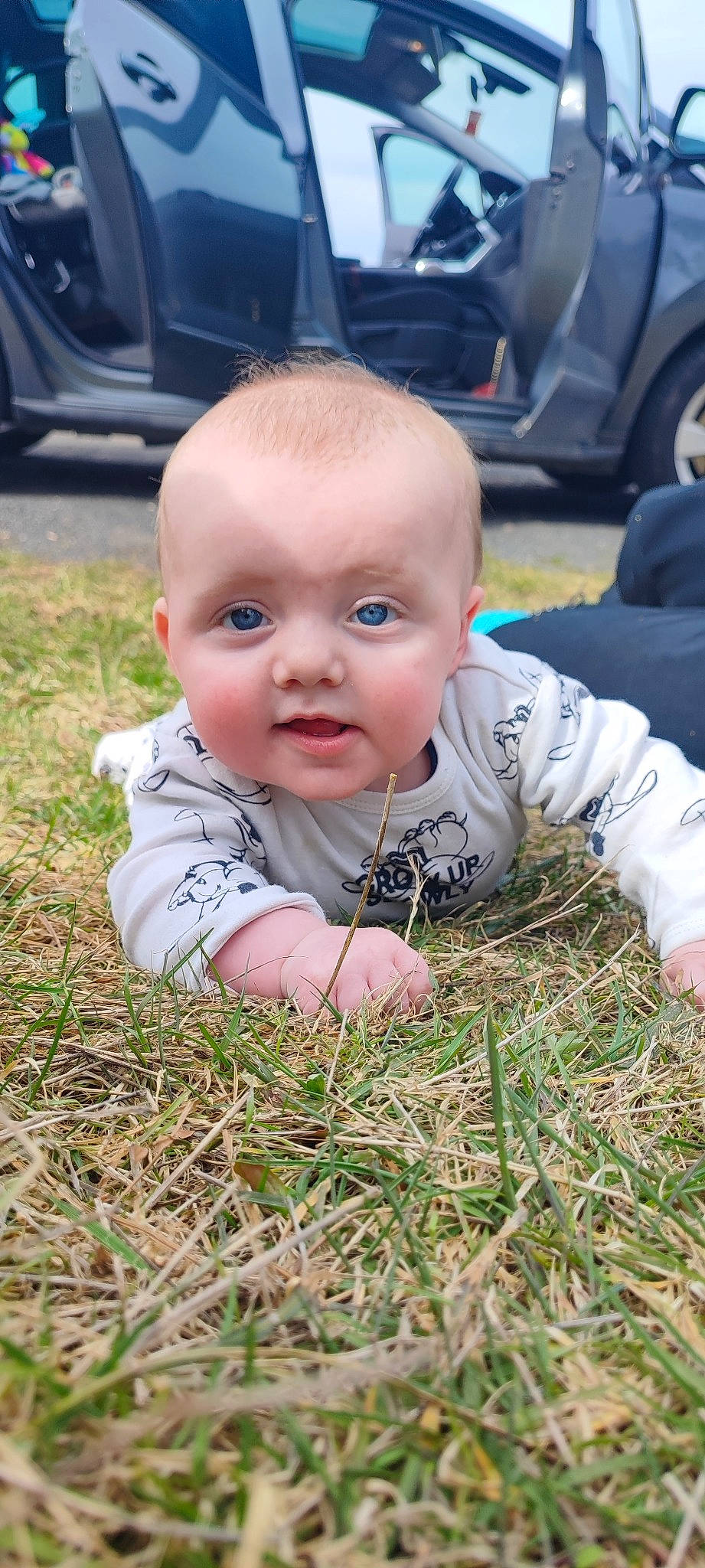 Maëlo a rejoint le concours — aidez-le/la à gagner de superbes lots ! automotive_tire, baby, baby_toddler_clothing, child, crawling, dress, flooring, grass, happy, head, lawn, mammal, people_in_nature, person, plant, skin, smile, tire, toddler, wheel