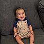baby, smiling, infant, sitting, couch, clothing, overall, happy, indoor, person, face, cute, child, short_sleeves, foot, skin, human, young, relaxed, home