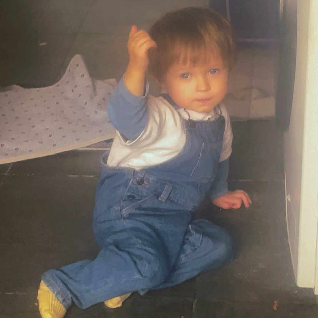 Malo a rejoint le concours — aidez-le/la à gagner de superbes lots ! baby, blue_clothing, casual, child, child_playing, crouching, curious_expression, floor, floor_cloth, home, indoor, kitchen, overalls, person, short_hair, small_child, tile_floor, toddler, white_shirt, young_child