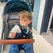 Malo a rejoint le concours — aidez-le/la à gagner de superbes lots ! baby, canopy, casual_clothing, child, curious, denim_overalls, floor, footwear, indoor, light, mirror, pacifier, person, reflection, safety_harness, seated, shopping_mall, striped_shirt, stroller, toddler