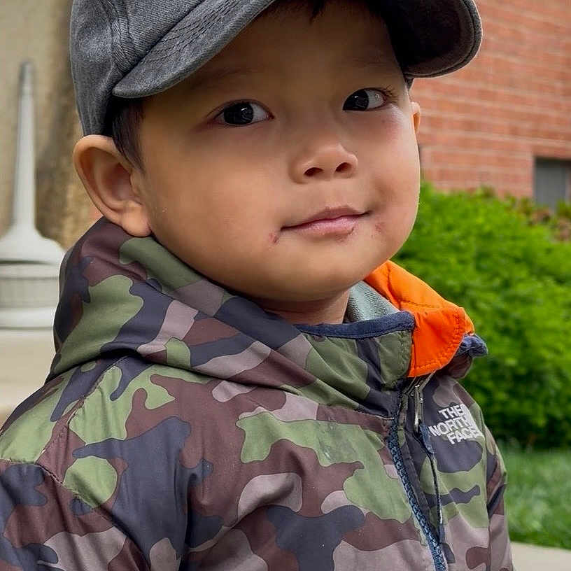 Samuel Sang joined the competition — help win amazing prizes! child, boy, cap, jacket, camo, camouflage, outdoor, smile, face, person, greenery, brick_wall, urban, young, portrait, casual, hooded_jacket, nature, curious, cute