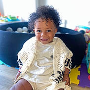 Neals a rejoint le concours — aidez-le/la à gagner de superbes lots ! toddler, child, smiling, curly_hair, knitted_cardigan, white_clothing, indoor, wooden_floor, play_area, ball_pit, happy, portrait, cute, sitting, young_child, person, bright_light, home, toy, casual_clothing