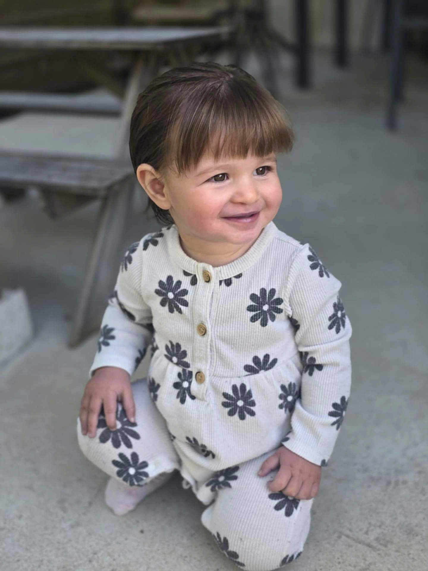 Emy a rejoint le concours — aidez-le/la à gagner de superbes lots ! toddler, child, smiling, kneeling, outdoor, concrete_floor, white_clothing, flower_pattern, long_sleeves, pants, brown_hair, cute, happy, person, portrait, casual, daylight, small_hands, buttoned_top, cozy_outfit