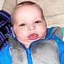 baby, infant, blue_clothing, gray_clothing, zipper, face, tongue, blanket, soft_texture, lying_down, close_up, child, cute, indoors, happy, person, toddler, smiling, skin, head