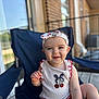 baby, child, smiling, headband, cherry, white_top, navy_chair, porch, wooden_floor, outdoor, sunlight, happy, cute, person, sitting, infant, summer, fashion, playful, closeup