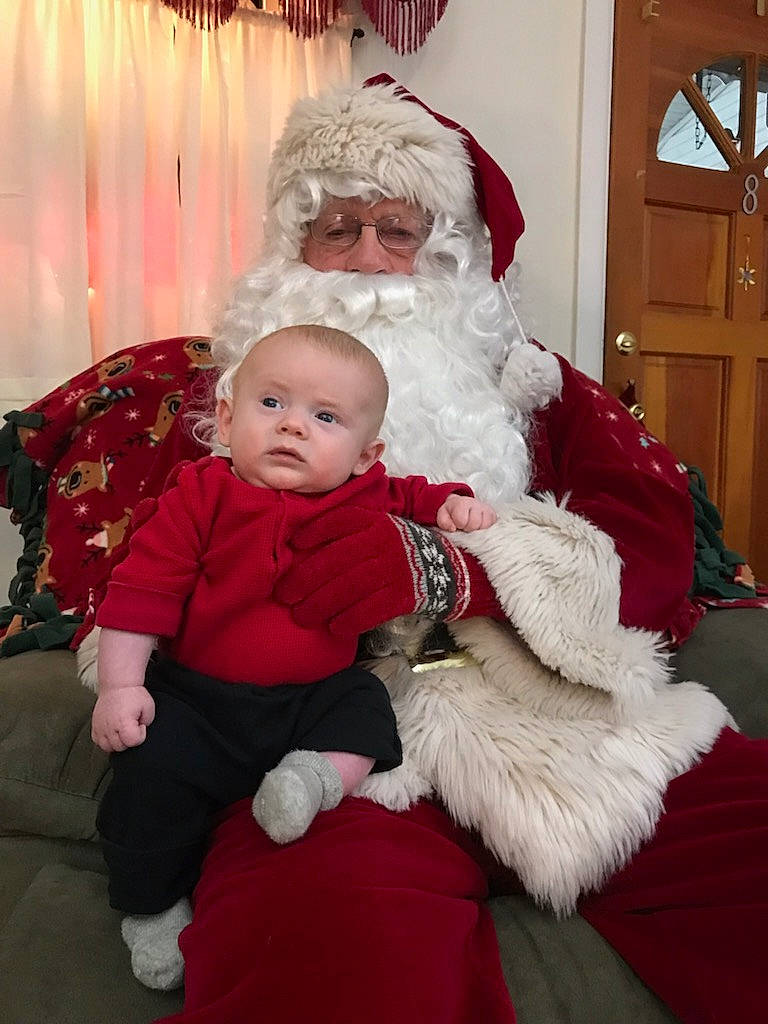 Jaxon is registered to the contest to win money with this photo: beard, christmas, christmas_decoration, comfort, door, event, face, facial_expression, facial_hair, fun, happy, hat, head, holiday, human_body, lap, person, santa_claus, standing, toddler