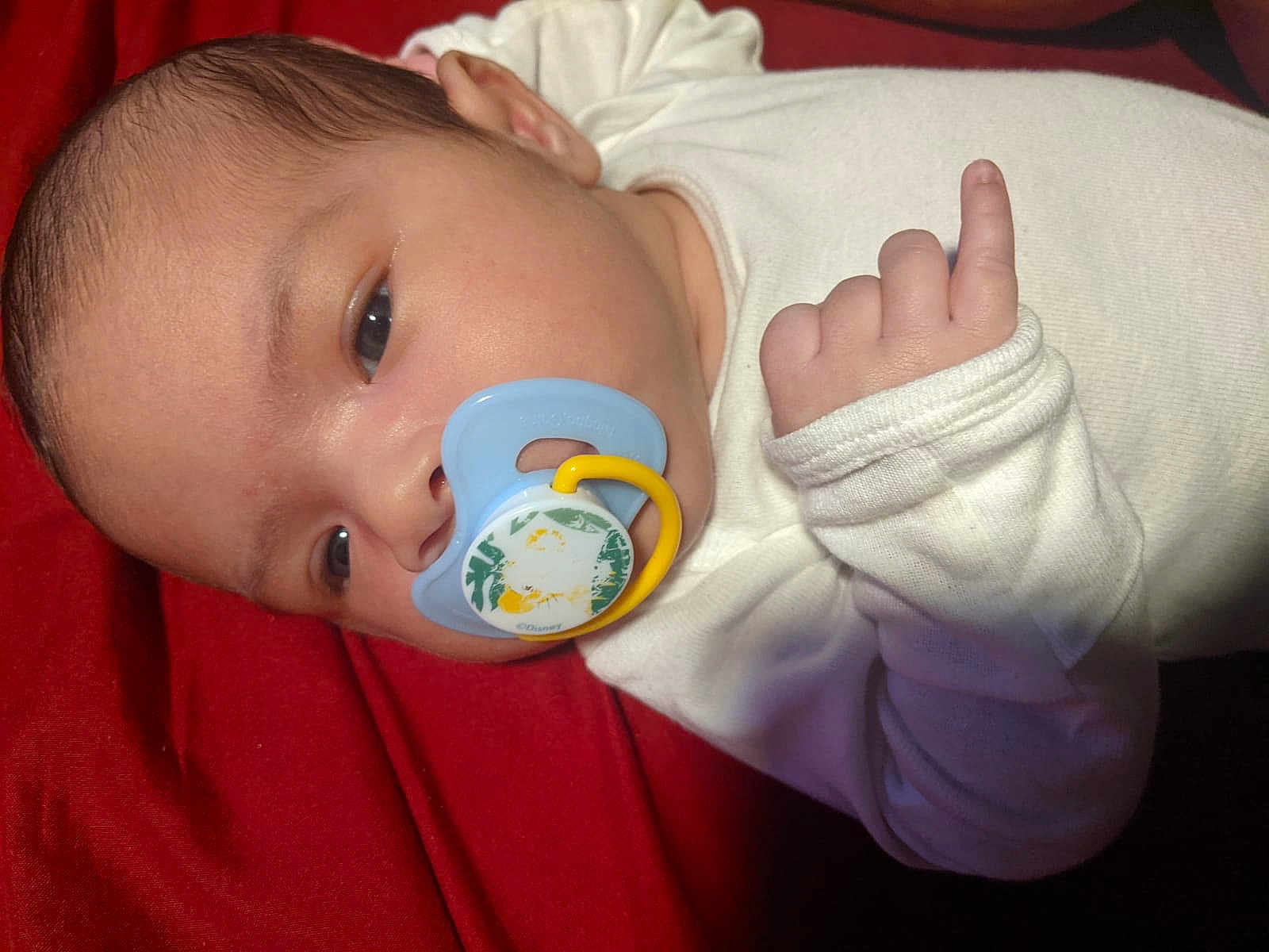 Kalel is registered to the contest to win money with this photo: baby, infant, pacifier, white_clothing, red_blanket, face, hand, close_up, sleepwear, newborn, cute, child, skin, portrait, calm, lying_down, indoor, soft_light, young, resting