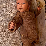 Jules a rejoint le concours — aidez-le/la à gagner de superbes lots ! baby, infant, knitted_clothing, brown_outfit, hat, blanket, fluffy, cat, pet, stretching, indoor, cozy, cute, child, newborn, portrait, laying_down, warm, soft_texture, relaxed