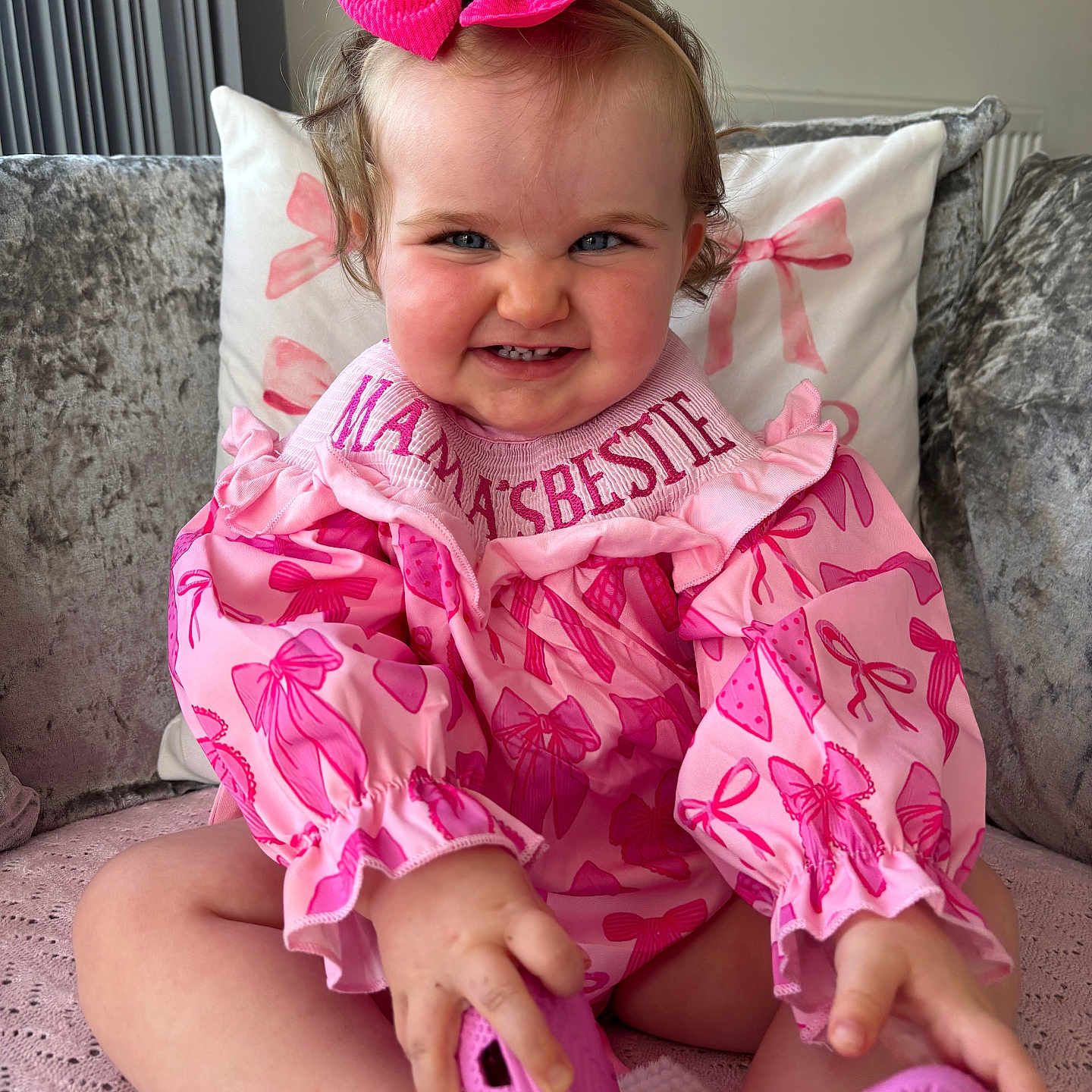 Darcey is registered to the contest to win money with this photo: baby, bow, child, clothing, couch, cushion, cute, face, footwear, hair, hand, happy, home, indoor, person, pink, playful, sitting, smile, toddler