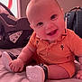 baby, child, smiling, orange_clothing, romper, sitting, indoor, bed, car_seat, backpack, footwear, happy, cute, infant, person, face, head, chubby_cheeks, short_hair, toy