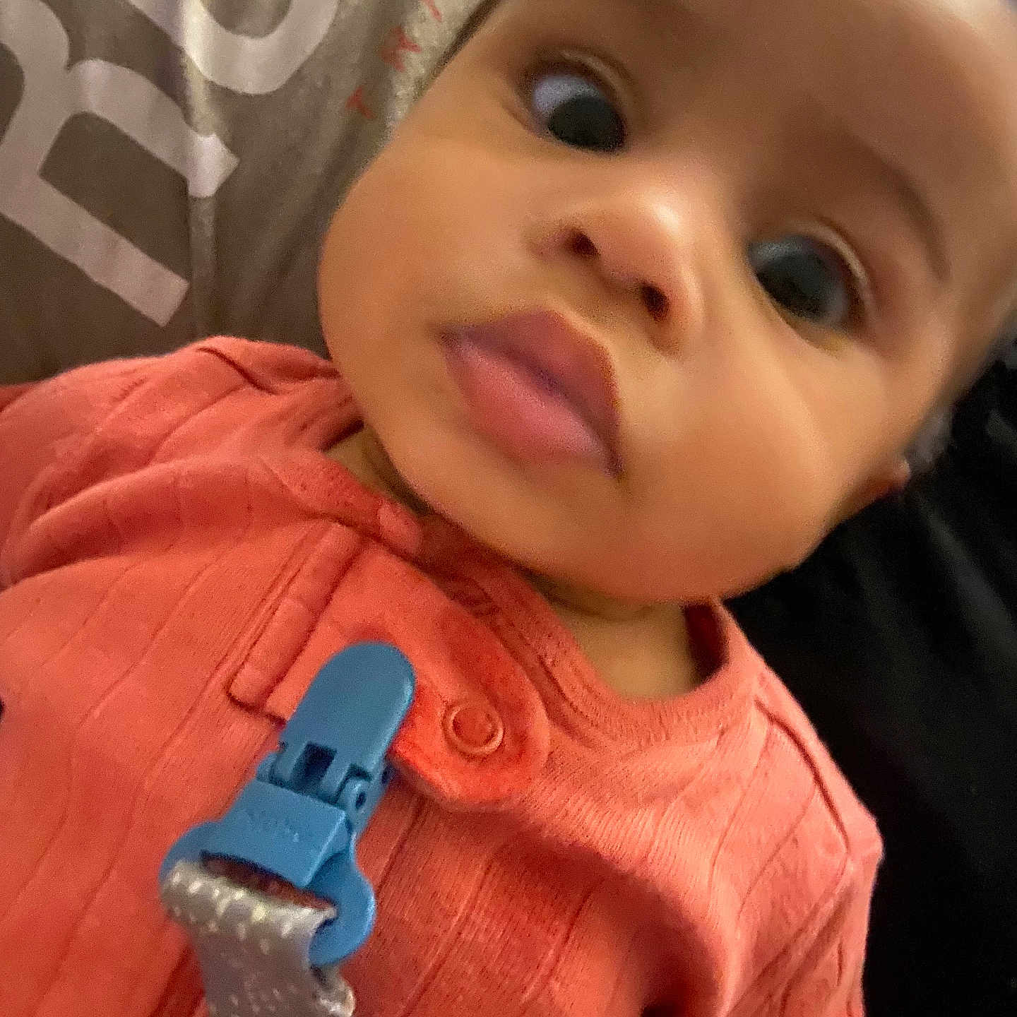 Elody is registered to the contest to win money with this photo: baby, blurred_background, child, close_up, clothing, coral_outfit, curious, cute, fabric, face, head, indoors, infant, pacifier_clip, person, portrait, skin, soft_lighting, wide_eyes, young