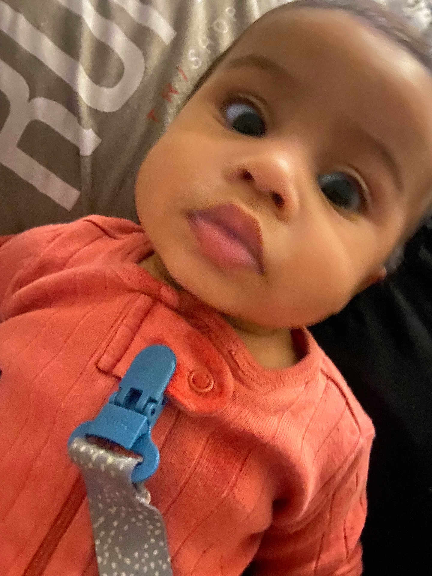 Elody is registered to the contest to win money with this photo: baby, close_up, infant, face, pacifier_clip, coral_outfit, curious, wide_eyes, indoors, soft_lighting, child, portrait, young, person, cute, clothing, fabric, blurred_background, skin, head