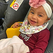 Elody joined the competition — help win amazing prizes! baby, smiling, headband, flower, bib, car_seat, child, blanket, yellow_purse, happy, cute, infant, clothing, portrait, indoors, person, seatbelt, accessory, face, toddler