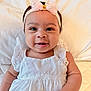 baby, infant, child, smiling, dress, headband, bow, white_clothing, cute, happy, portrait, laying_down, soft_blanket, indoors, skin, face, eyes, mouth, hand, adorable