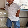 toddler, child, indoor, smiling, white_shirt, jeans, sneakers, standing, couch, window, natural_light, face, person, casual_clothing, happy, young_child, home, portrait, fashion, cute