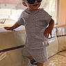 toddler, child, sunglasses, gray_outfit, shorts, hoodie, sneakers, nike, indoor, couch, smile, standing, fashion, cute, person, footwear, black_socks, reflection, window, light