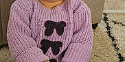 Victoire a rejoint le concours — aidez-le/la à gagner de superbes lots ! baby, child, sitting, purple_sweater, yellow_bow, pony_tail, blue_eyes, carpet, toy_comb, socks, bear_face, indoor, furniture, curious_expression, cozy_clothing, hands, floor, playful, cute, person