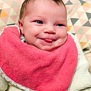Victoire a rejoint le concours — aidez-le/la à gagner de superbes lots ! baby, infant, smile, tongue, pink_bib, white_outfit, face, head, cushion, patterned_background, closeup, cheeky, cute, child, newborn, happy, indoors, soft_texture, cozy, portrait