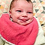 baby, infant, smile, tongue, pink_bib, white_outfit, face, head, cushion, patterned_background, closeup, cheeky, cute, child, newborn, happy, indoors, soft_texture, cozy, portrait
