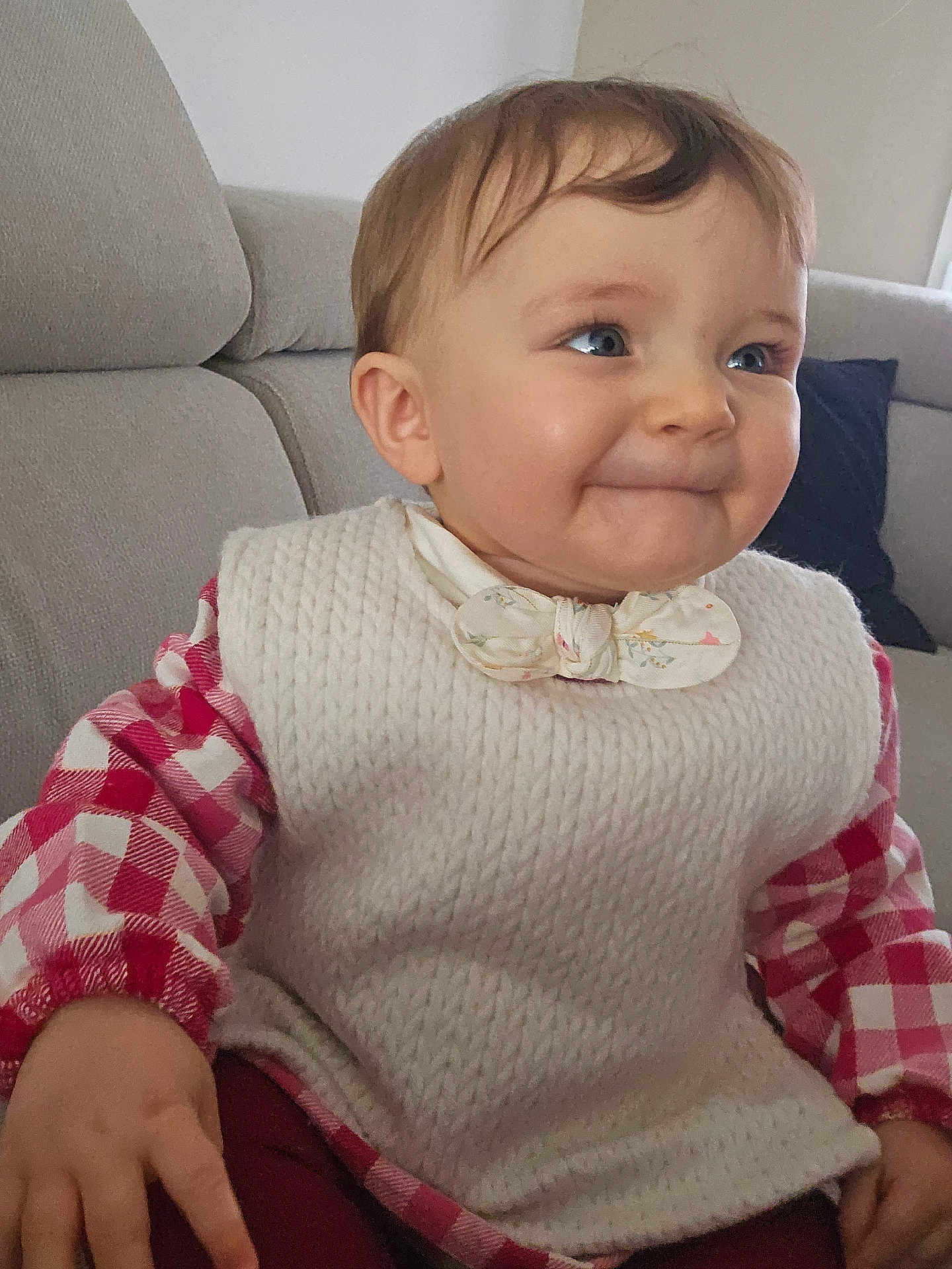 Victoire participe au concours pour gagner de l'argent avec cette photo : baby, child, infant, smiling, sitting, knitted_vest, checkered_shirt, couch, indoor, happy, face, expression, person, clothing, toddler, homedecor, furniture, portrait, cute, young
