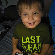 Jonathan is registered to the contest to win money with this photo: child, smiling, controller, video_game, indoor, casual_clothing, green_shirt, messy_face, happy, playing, young_child, person, short_hair, bed, chair, furniture, dim_lighting, candid, closeup, portrait